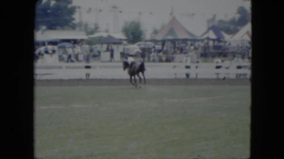 1951 Cleveland fair scene showing a rider on a dark horse near a white rail, with tents, spectators, and mid-century cars beyond the field.