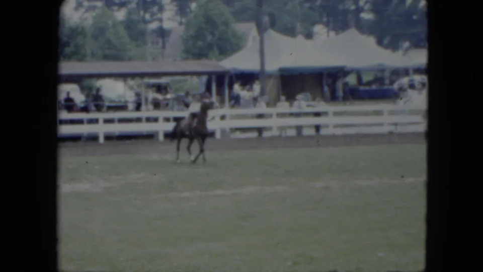 A helmeted rider on a dark horse passes nearer the camera in the 1951 Cleveland outdoor arena, with tents and spectators behind.