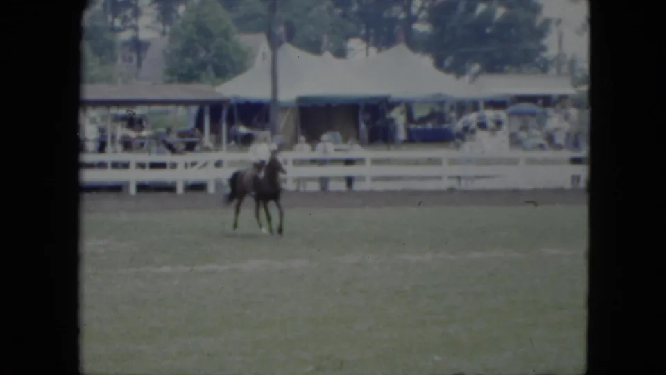 The horse and rider angle across the grassy Cleveland arena as the white fence, tented spectator area, and trees remain in view.