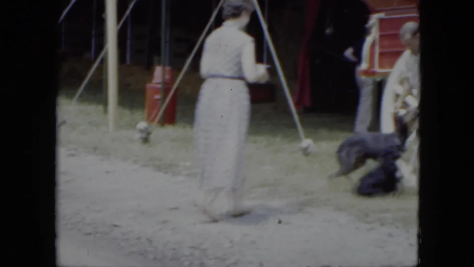 1951 Cleveland home-movie frame showing a woman passing circus handlers and dogs near tent poles and a red wagon.