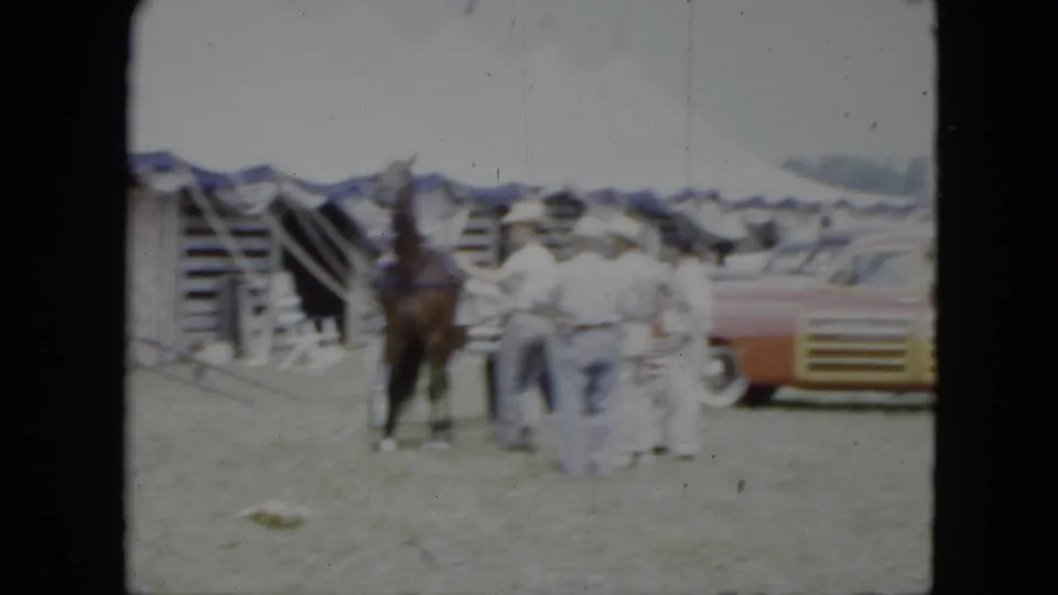 1951 Cleveland home-movie frame showing a horse near handlers, tents, crates, and cars at a circus setup area.