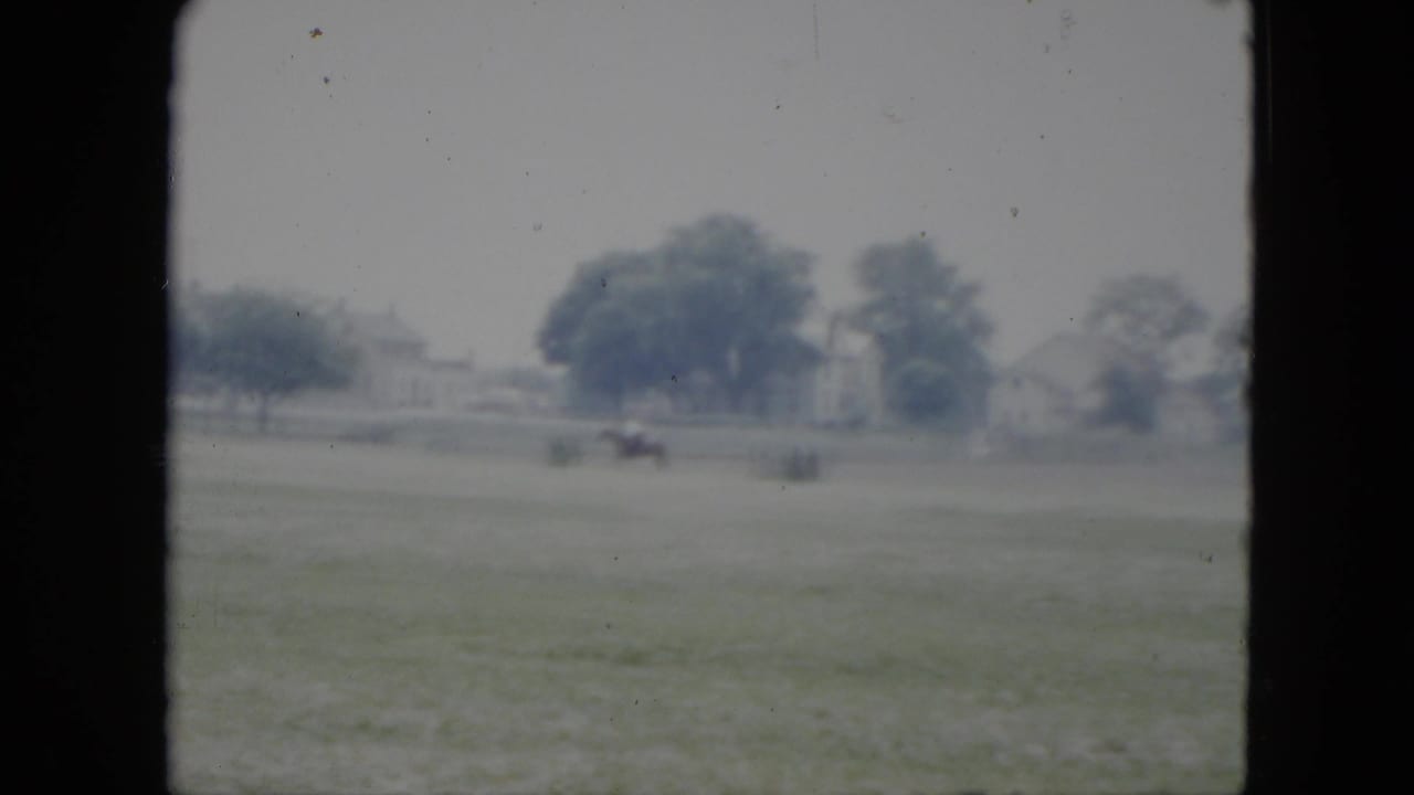 Distant horseback rider in a grassy Cleveland field, with trees and houses in the soft 1951 8mm background.