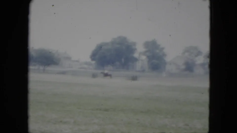 Distant horseback rider in a grassy Cleveland field, with trees and houses in the soft 1951 8mm background.