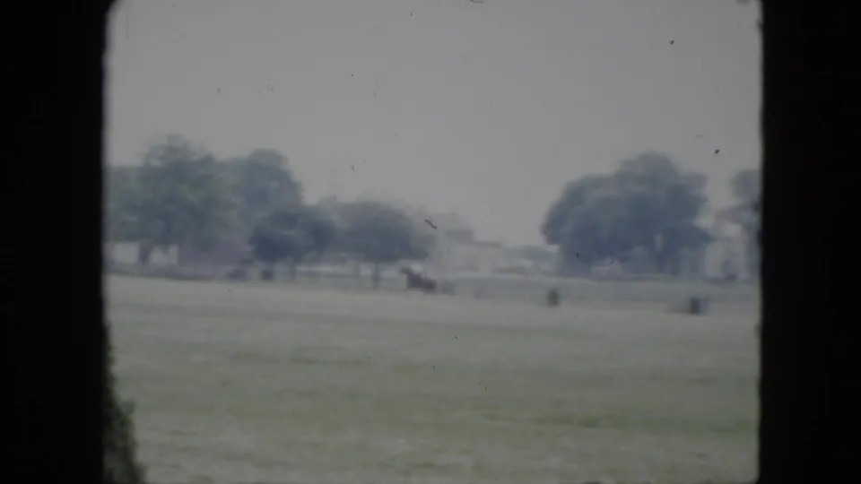 Wide 1951 Cleveland field view with a distant horseback rider, scattered objects, trees, and neighborhood houses.