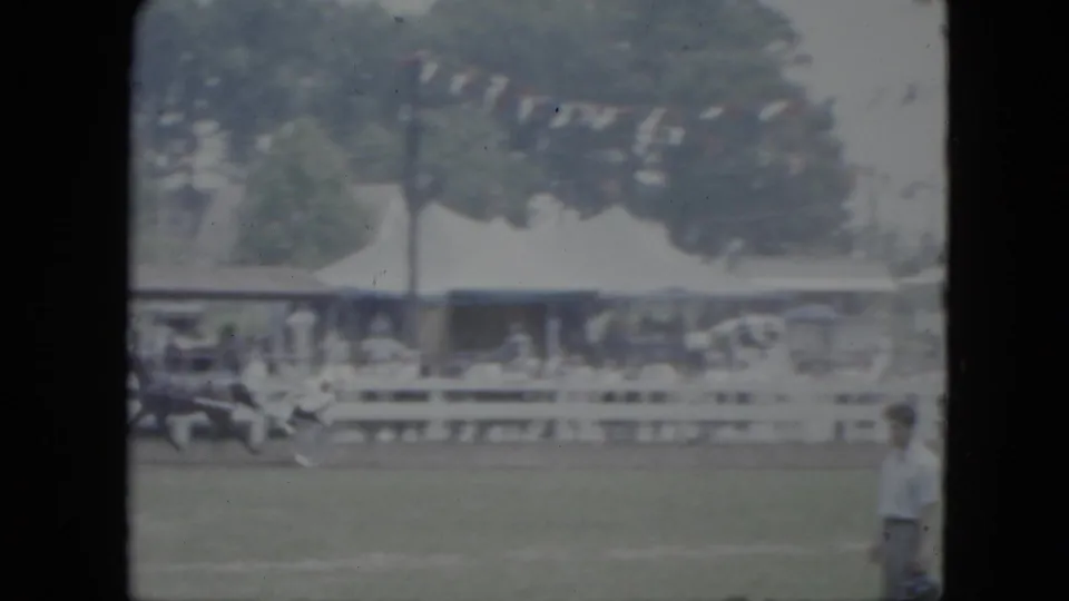 Soft 8mm frame from Cleveland in 1951 showing a horse-drawn sulky passing a fence line with spectators and bunting in the background.