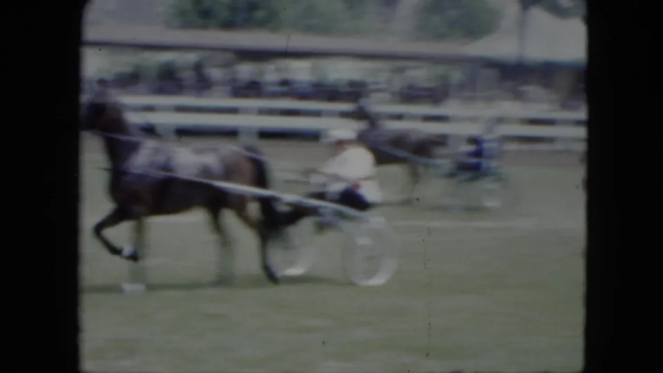 Soft 8mm frame from 1951 Cleveland showing a harness horse and sulky driver in motion blur on a grassy fairground track.