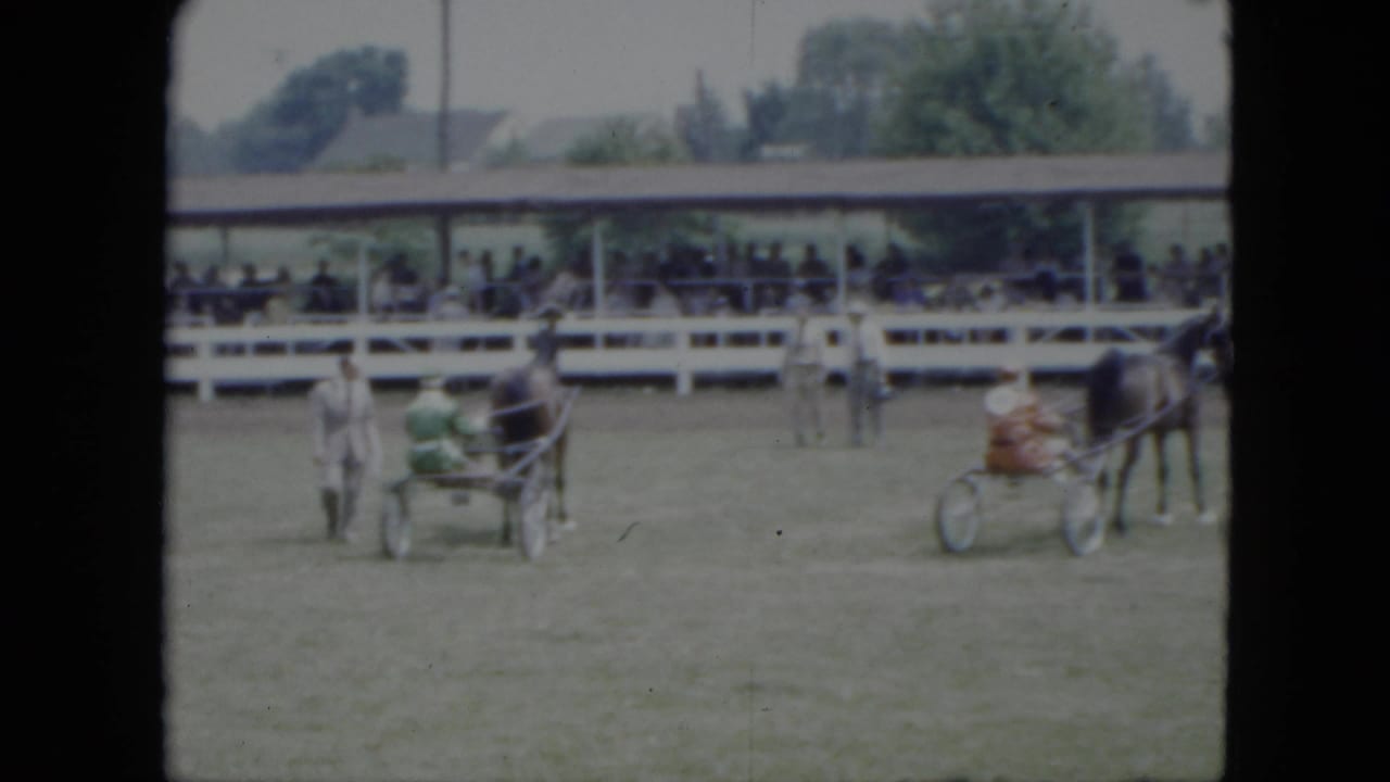 1951 Cleveland-area home movie frame showing harnessed horses and small carriages moving across a fairground arena before spectators.