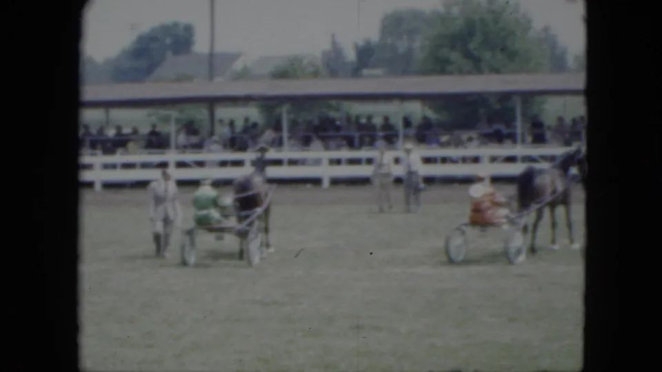 1951 Cleveland-area home movie frame showing harnessed horses and small carriages moving across a fairground arena before spectators.