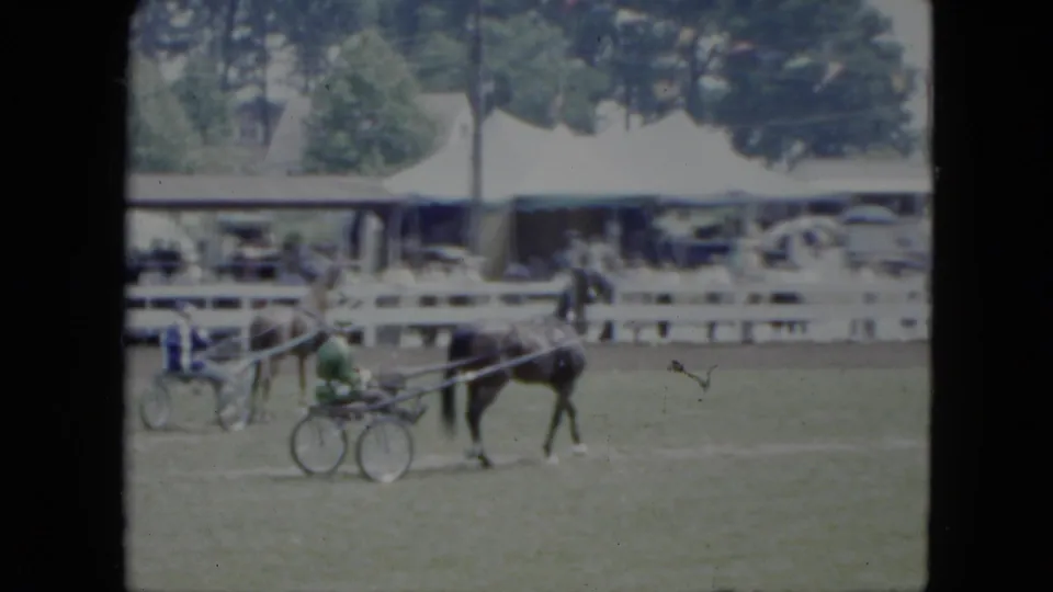 1951 Cleveland frame showing a horse-drawn sulky on a grass track, with spectators, parked cars, trees, and a white fence in the background.