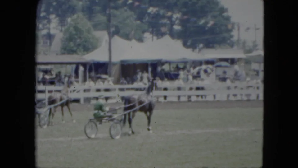1951 Cleveland 8mm frame showing a harness horse and green sulky moving past a white fence, tents, and spectators.