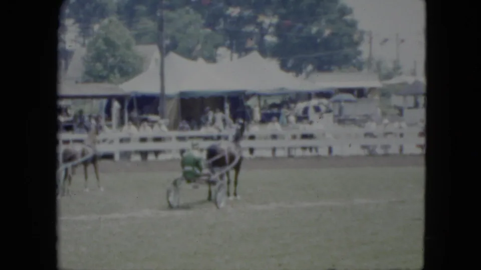 A green-clad driver in a sulky follows a harness horse at a Cleveland fairground or track in 1951.