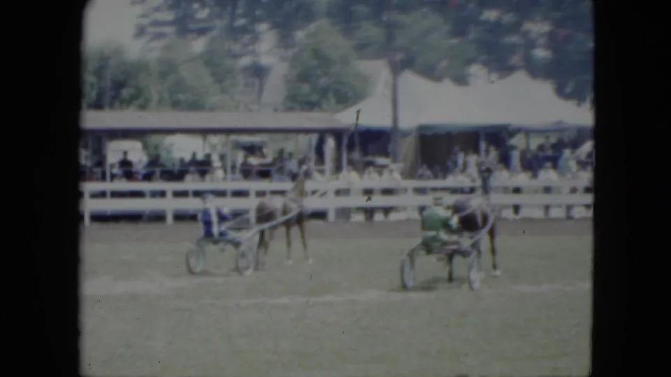 Two harness racers in blue and green appear on the grass track during a 1951 Cleveland home-movie scene.