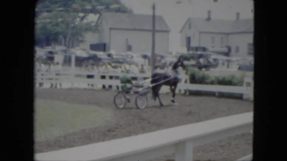 Near the end of the clip, the horse and sulky pass the camera position on the Cleveland fairground track with cars and buildings behind the fence.