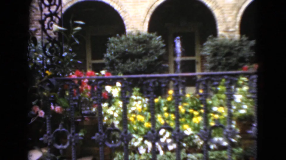 1952 Florida courtyard view showing wrought-iron railing, colorful flowers, shrubs, and arched masonry openings in soft 8mm color.