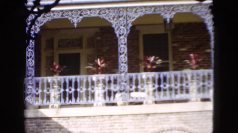 1952 Florida residential exterior showing decorative white porch ironwork, brick walls, windows, and potted plants.