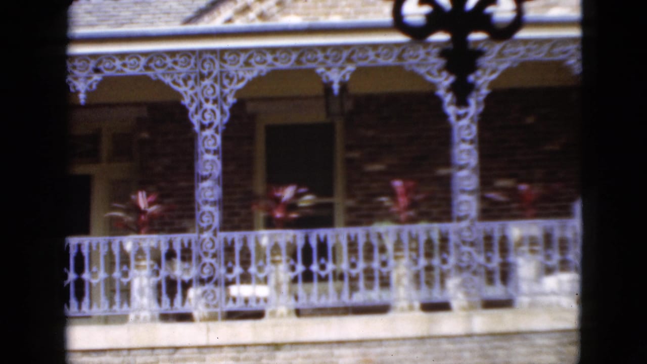 1952 Florida home-movie frame of a brick balcony facade with white decorative railings, shaded openings, and potted plants.