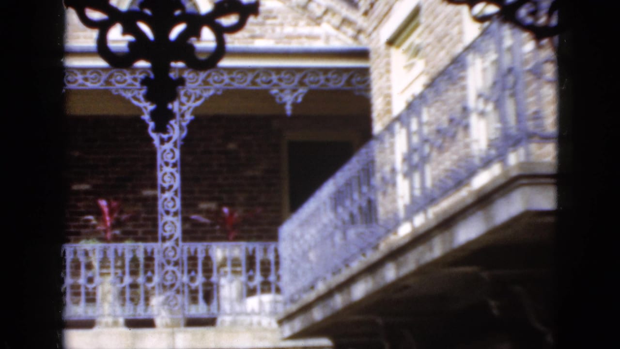 1952 Florida 8mm frame showing a brick apartment facade with decorative white iron balcony railings and shaded porch detail.