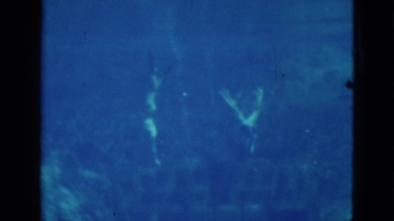 Blue-tinted underwater 8mm frame from the Florida spring, with faint swimmer forms visible behind dark frame borders.