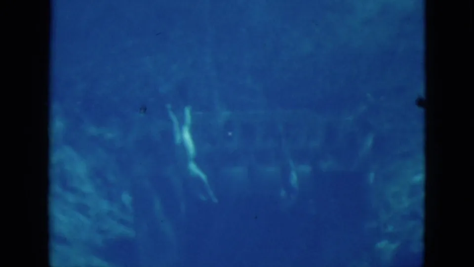 Blue underwater 8mm frame showing several faint swimmers or divers in the Florida spring near dark film borders.