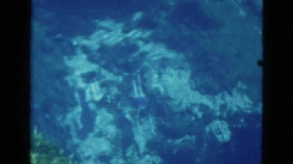 1952 Florida 8mm frame showing two underwater swimmers with fins, softened by water depth, grain, and blue color shift.