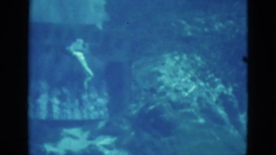 1952 Florida 8mm frame showing a swimmer silhouette in deep blue water with rock forms and bubbles below.