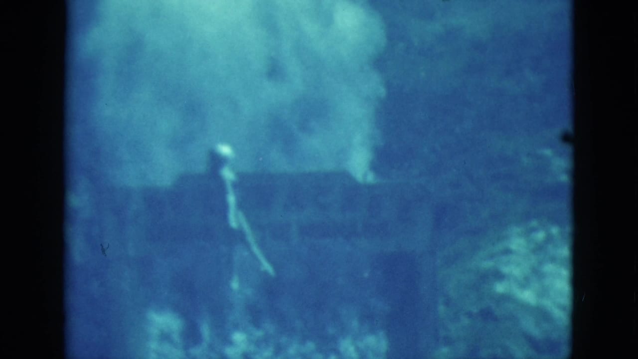 1952 Florida 8mm underwater frame showing a swimmer in blue water near coral-like formations and suspended particles.
