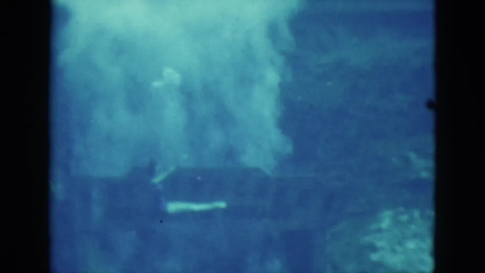 1952 Florida 8mm underwater frame with blue water, reef-like forms, and a pale swimmer or sea-life shape in soft focus.