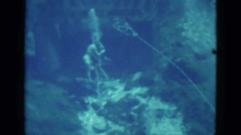 1952 Florida 8mm frame showing a scuba diver in blue-green water near reef-like rock, with soft focus and dark frame borders.