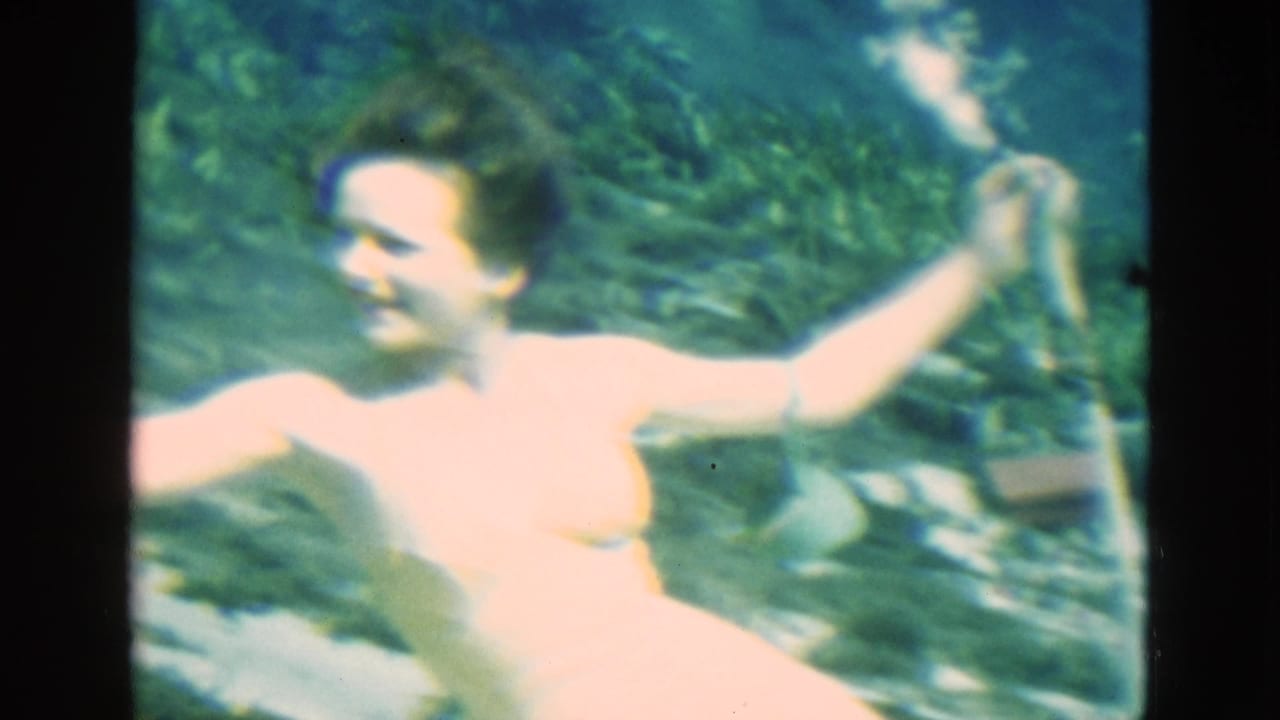 Woman in a pale swimsuit swims underwater while holding a breathing tube.
