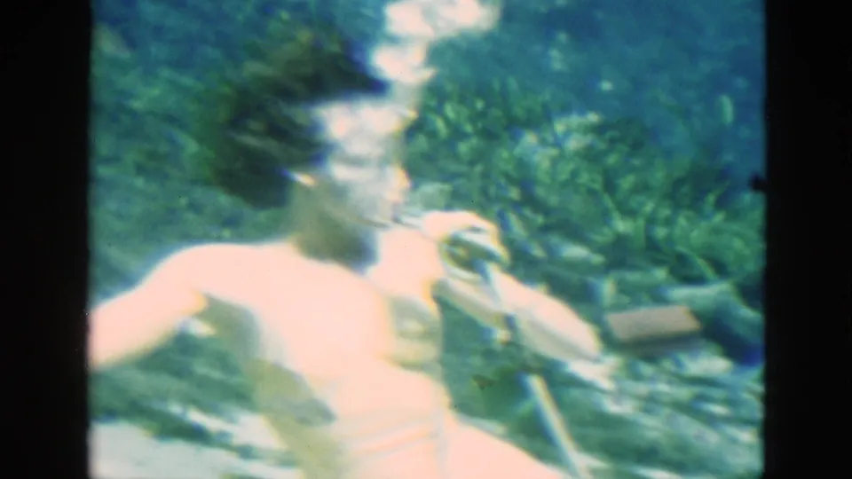 The swimmer turns underwater in the Florida footage, with bubbles near her face and a breathing tube visible against the green spring background.