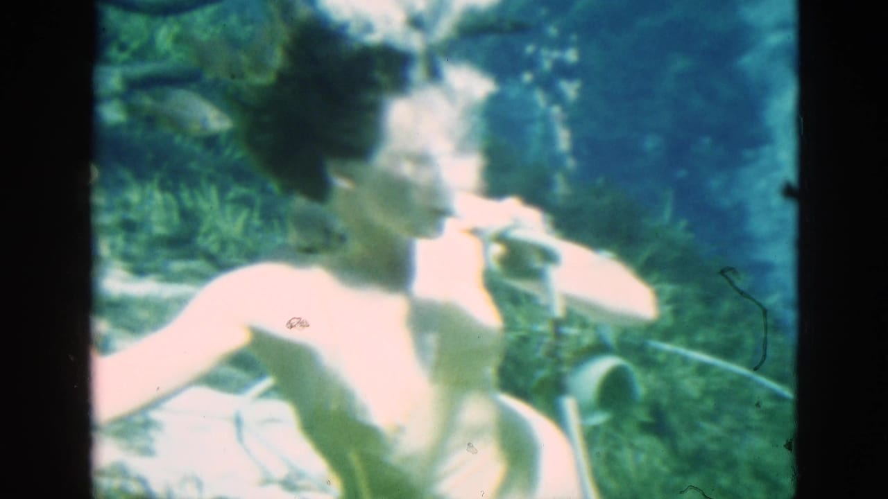 1952 Florida 8mm frame of an adult woman underwater in swimwear, holding an air tube as fish and plants appear around her.