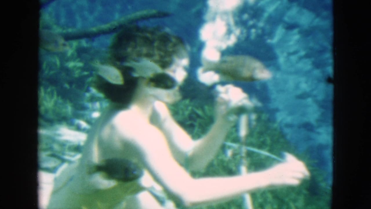 Woman underwater brings an air tube to her mouth while a fish swims nearby.