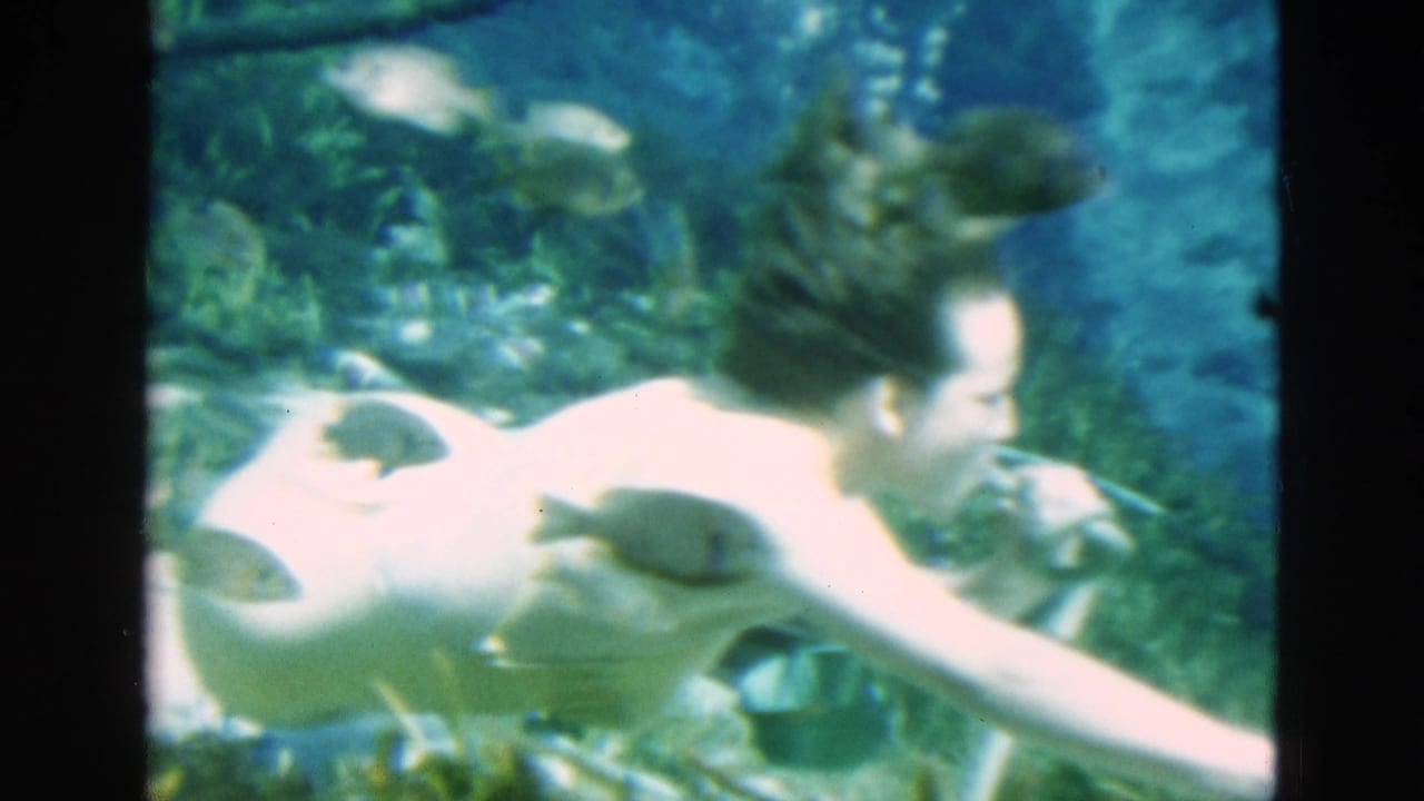 1952 Florida home-movie frame showing an adult woman swimming underwater, with floating hair, fish, and spring vegetation visible.