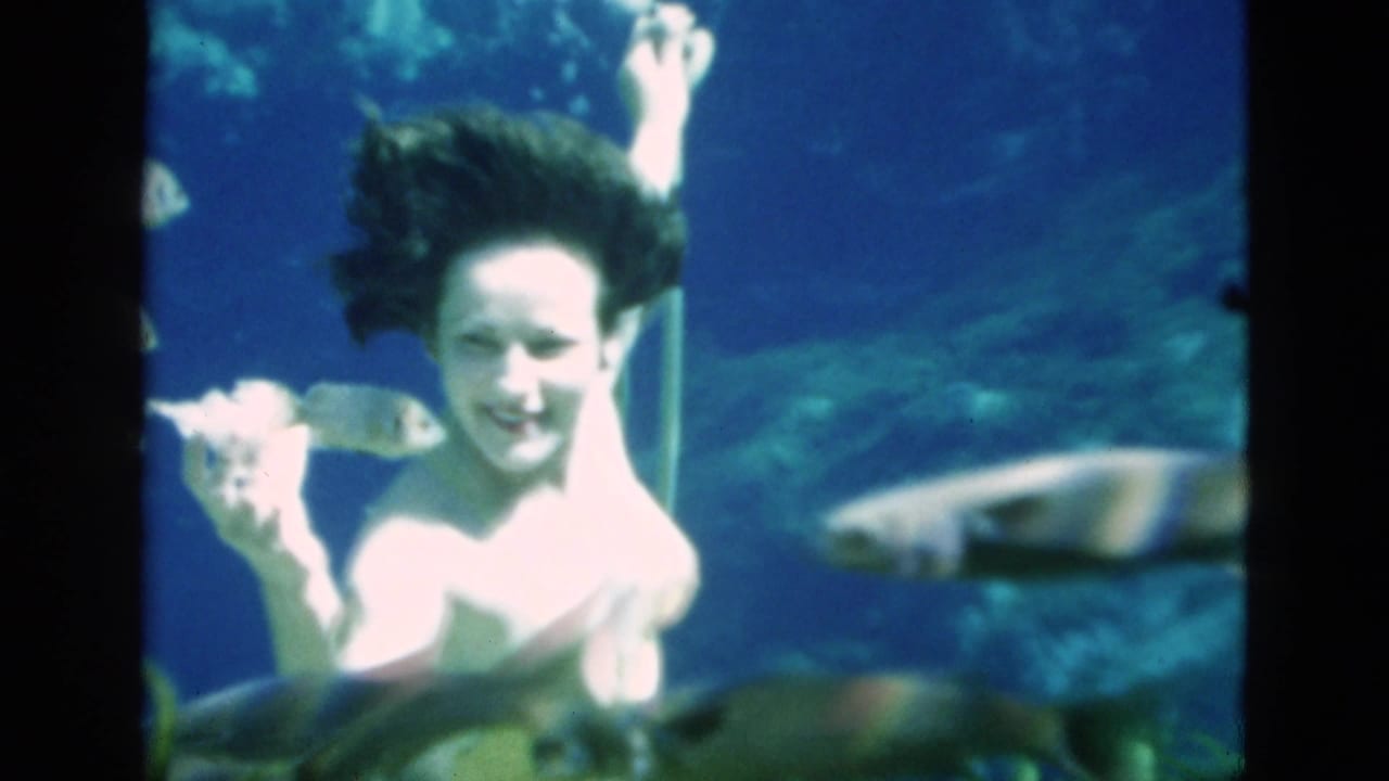 In 1952 Florida home-movie footage, a woman in a light swimsuit smiles underwater with fish and blue water around her.