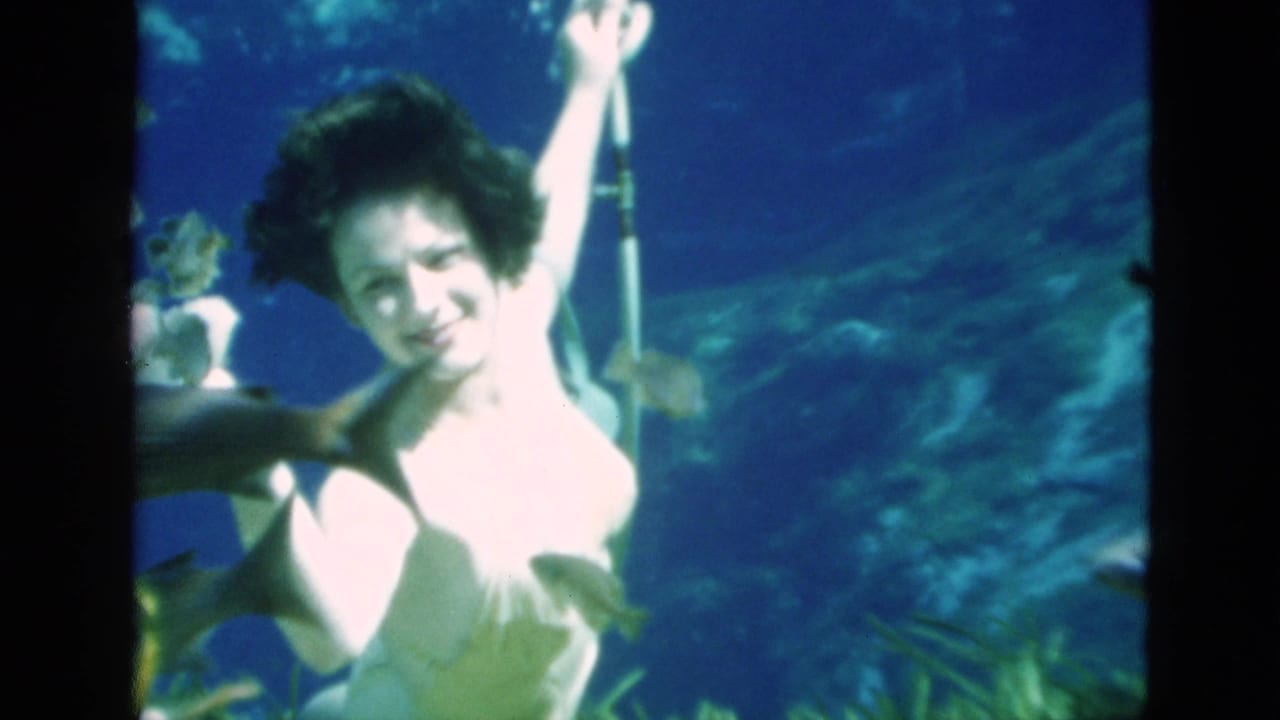 Woman underwater holding a vertical pole while fish swim nearby.