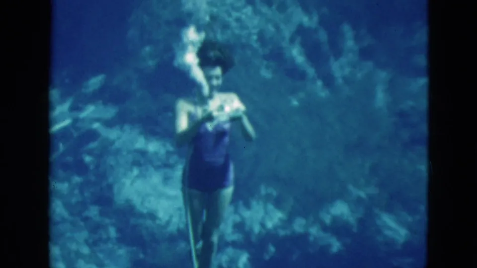 The swimmer holds the hose close while bubbles rise in the blue underwater Florida home-movie frame.