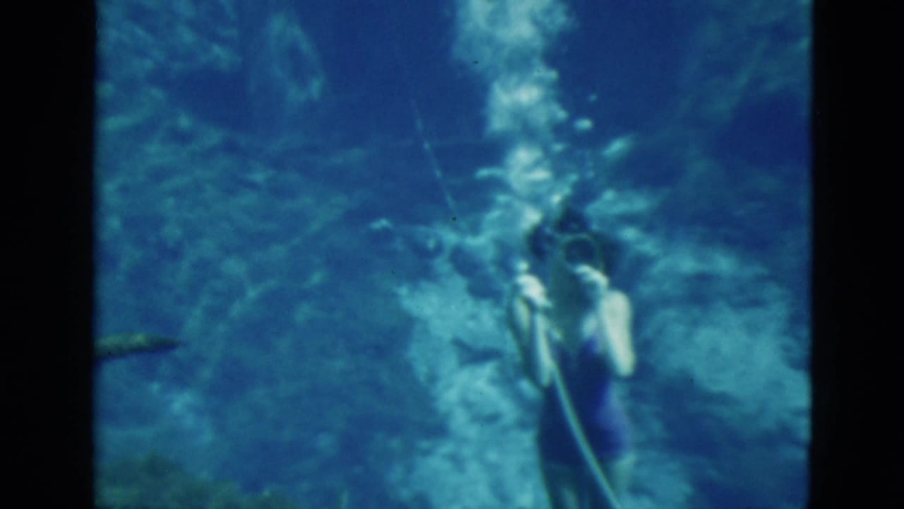 1952 Florida 8mm frame of two young women underwater with swim fins, masks and visible air hoses in blue-green water.