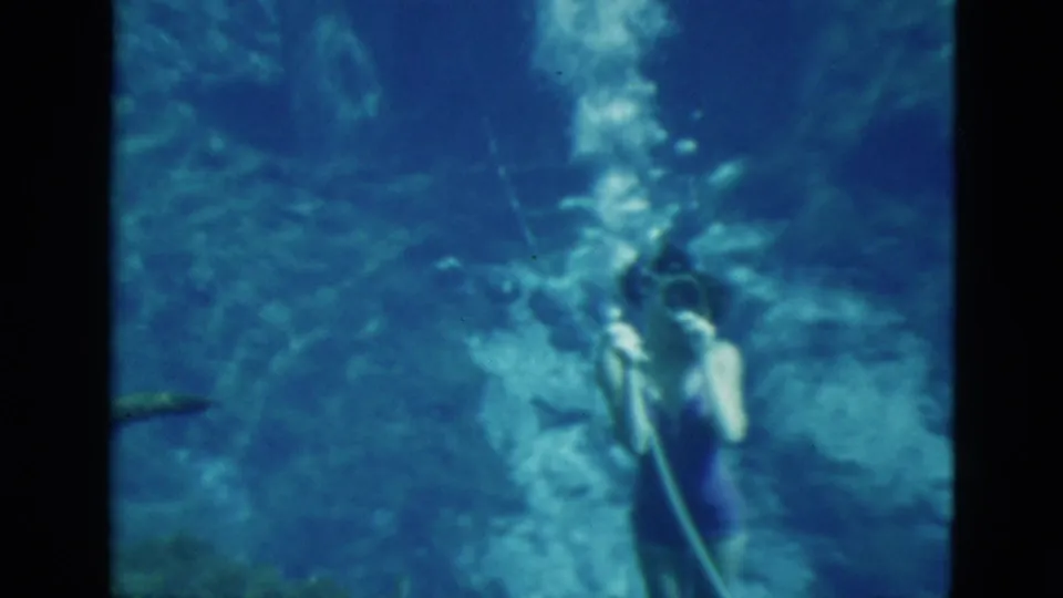 1952 Florida 8mm frame of two young women underwater with swim fins, masks and visible air hoses in blue-green water.