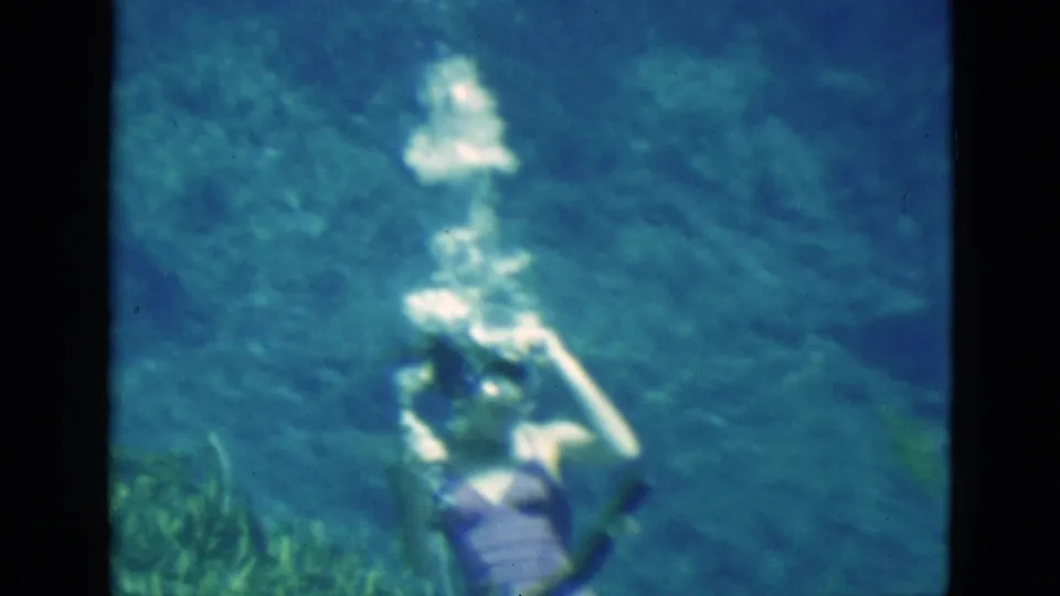 1952 Florida 8mm frame showing a woman in a purple swimsuit underwater as bubbles rise around her head.