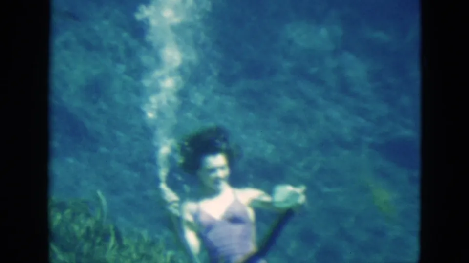 1952 Florida 8mm frame of a woman underwater in a purple swimsuit, with bubbles rising in clear blue-green water.