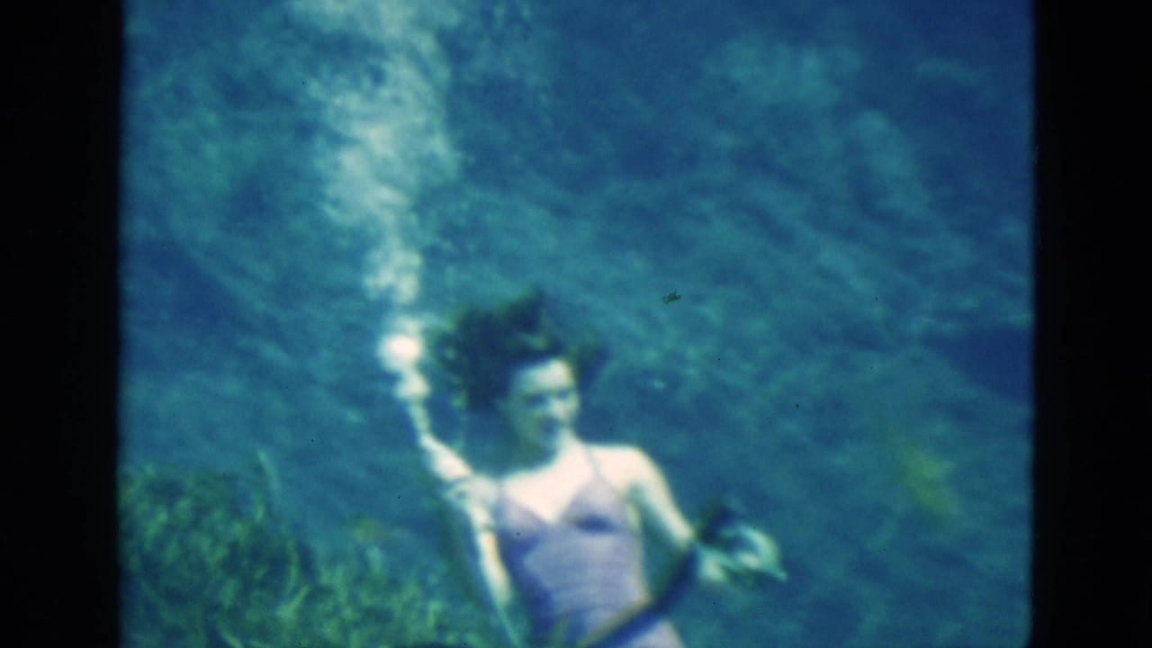 Woman underwater in a purple swimsuit holding an air tube as bubbles rise beside her.