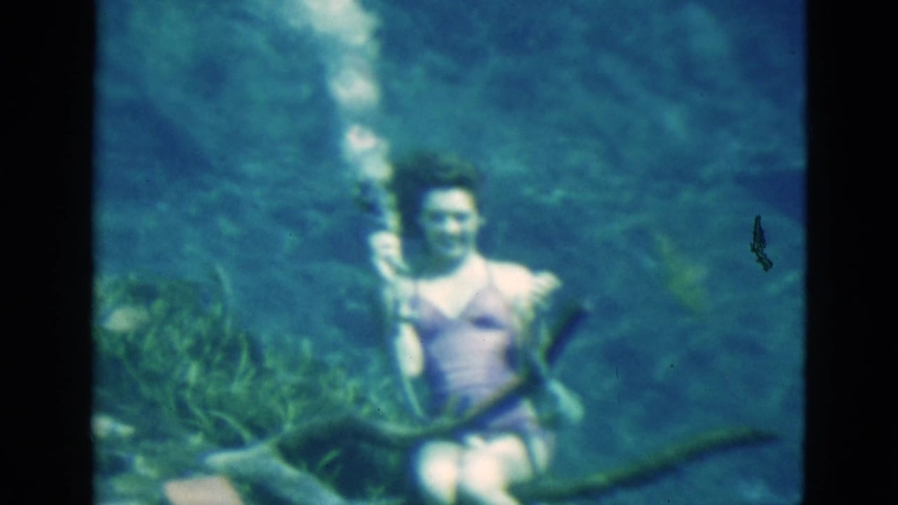 1952 Florida home-movie frame showing a smiling woman underwater with a breathing tube, surrounded by blue-green water and aquatic plants.