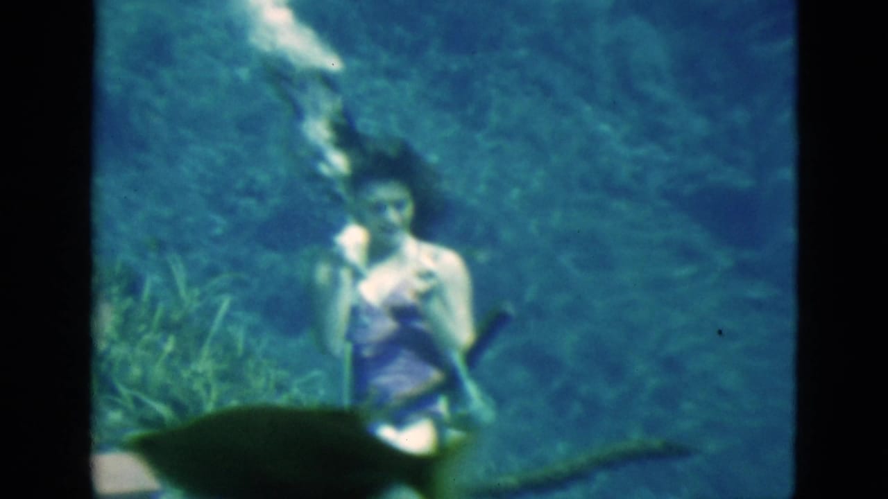 Woman underwater holds a vertical air tube with bubbles rising above her head.