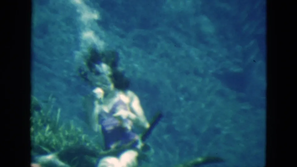 1952 Florida home-movie frame of a woman underwater, with bubbles near her face and aquatic growth visible in front of her.