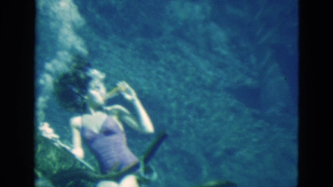 1952 Florida home-movie frame showing a woman underwater in a purple swimsuit raising a bottle near her mouth.