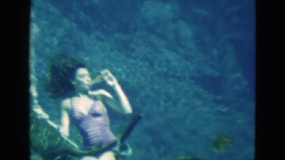 1952 Florida home-movie frame of a woman underwater in a purple swimsuit appearing to sip from a bottle.
