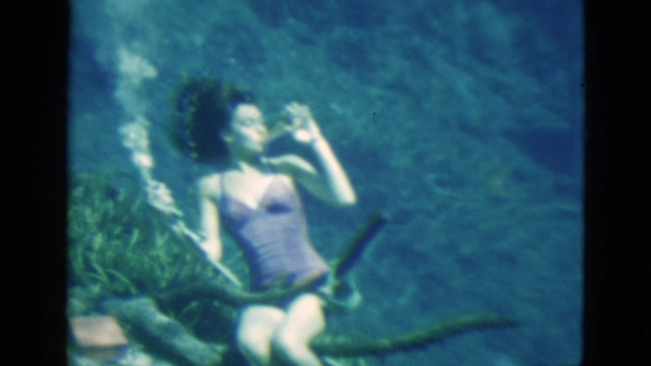 Woman underwater tilts a glass to her mouth as her hair floats upward.