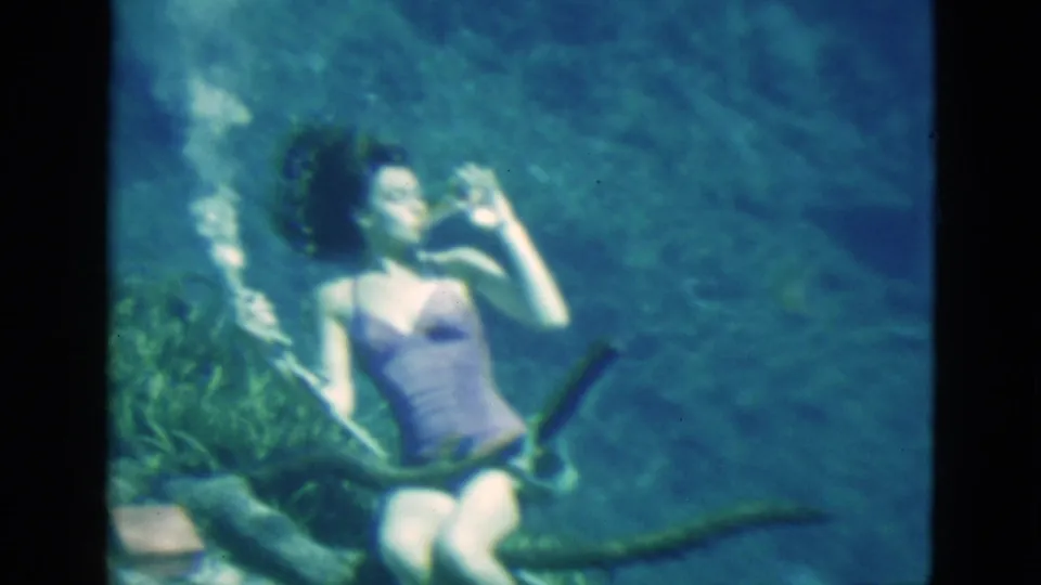 1952 Florida 8mm frame showing a woman underwater drinking from a glass, with floating hair, bubbles, plants, and blue-green water.