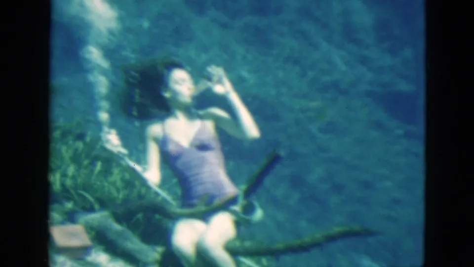 1952 Florida 8mm frame showing the woman underwater with a glass near her mouth, hair drifting and plants visible in the foreground.