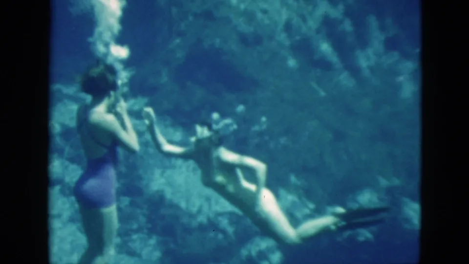 1952 Florida 8mm frame with two women underwater, one in a purple suit at left and another swimming nearby amid bubbles and blue water.